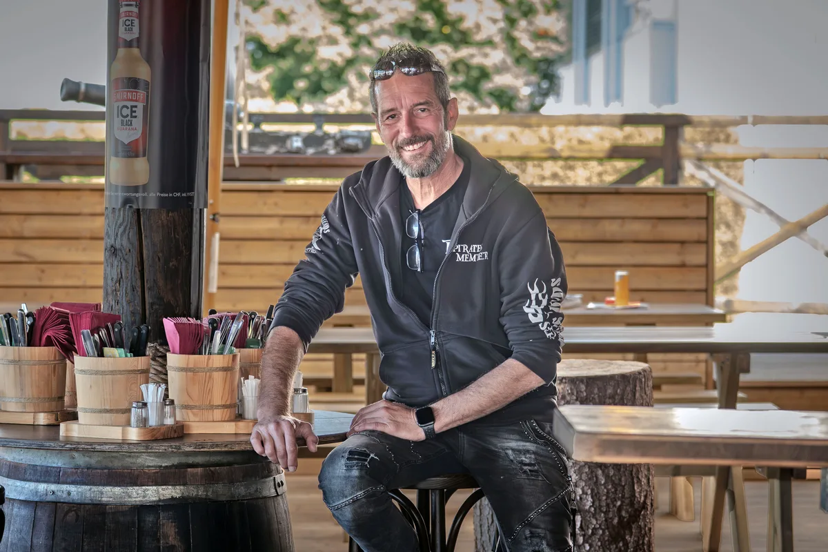 «Ich kenne den Letzigrund von vielen Events»: Päde Hofstetter ist zuversichtlich, das Restaurant zum Schlachthof rentabel führen zu können. Päde Hofstetter sitzt auf einem Barhocker und stützt sich auf eine Tischplatte. Er trägt schwarze Jeans, ein schwarzes Shirt und ein schwarzes Hoodie. Er trägt einen Bart und eine Sonnenbrille im Haar sowie eine Lesebrille im V-Ausschnitt des Shirts.